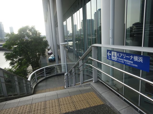 横浜駅からKアリーナ横浜のアクセス（日産グローバル本社ギャラリー入口前にあるKアリーナ横浜の矢印案内と高島水際線プロムナードに行く階段）