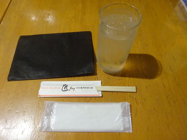 横浜ポルタ「匠 Jang」店内テーブルの上に置かれたお水、割りばし(お店の店名が書いてある)、手拭き、紙エプロン