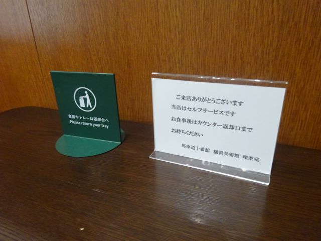 横浜美術館のカフェ「馬車道十番館 横浜美術館 喫茶室」のテーブル席に置かれた、食事後はカウンター返却口までお持ちくださいと書かれた案内