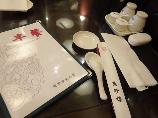 横浜中華街「萬珍樓點心舗」のテーブル席の様子（朝食用メニュー表、卓上調味、萬珍樓と書かれた箸袋など）