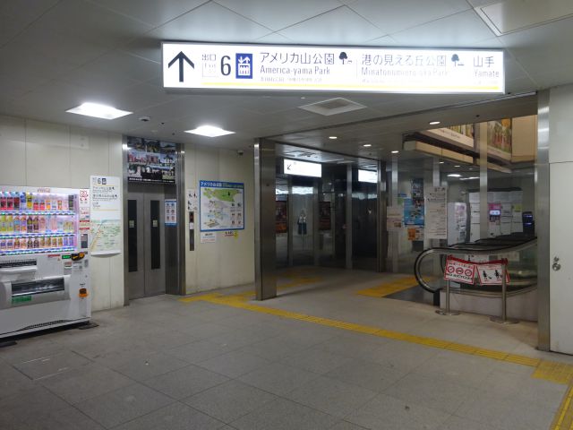 「港の見える丘公園」最寄り駅からの徒歩ルート（元町・中華街駅の元町改札を出たところにある出口6のエレベーター、エスカレーターの様子、頭上の看板に出口6アメリカ山公園・港の見える丘公園・山手と書いてある）